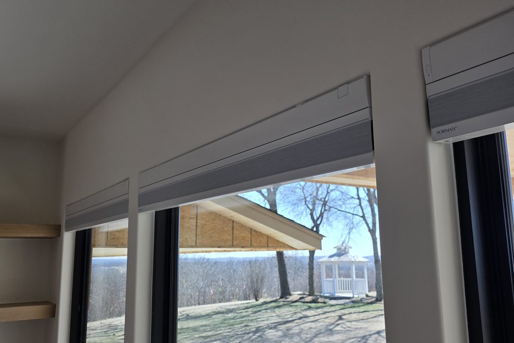 Roller shade installed on an angled skylight-style window with a countryside view